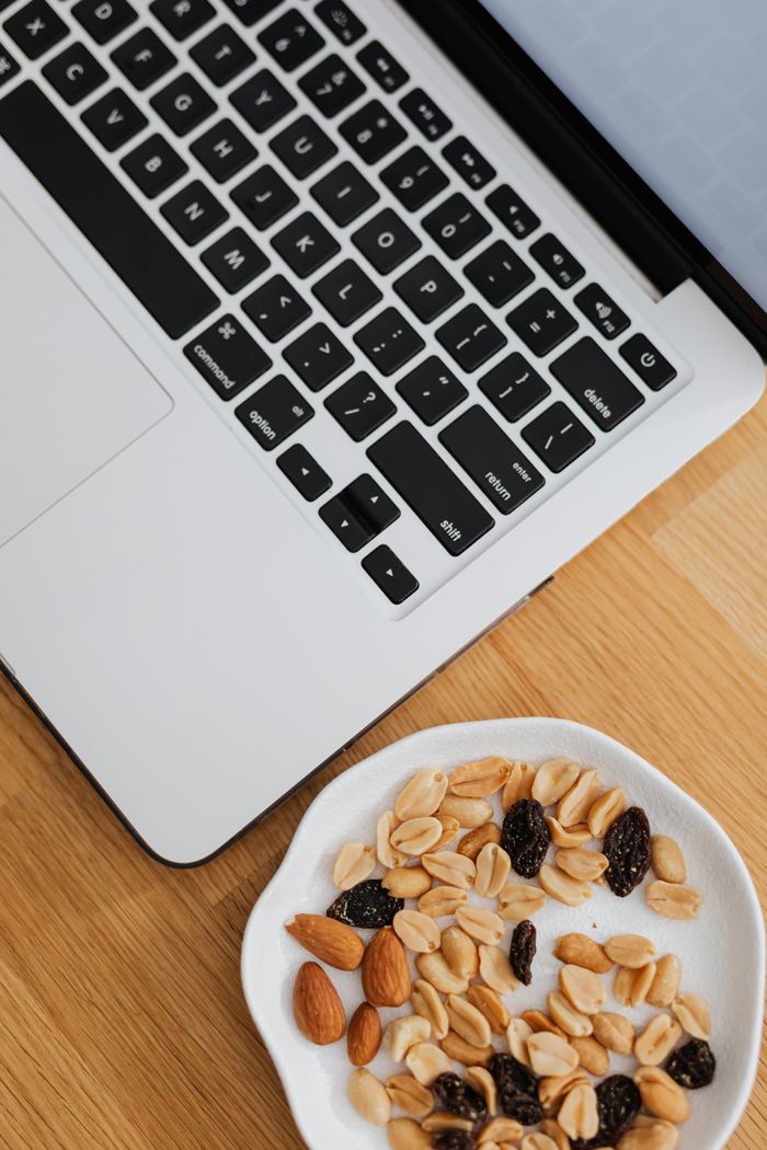 gallery-2 Plate of almonds, peanuts, and raisins beside open laptop. Perfect for work-from-home snack inspiration.