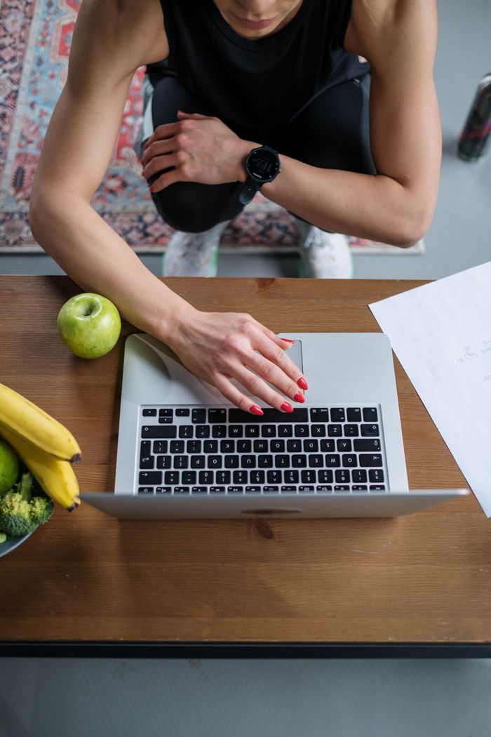 gallery-1 Overhead view of a woman using a laptop surrounded by fruits and documents.